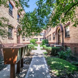 a walkway between two brick buildings with green grass and trees