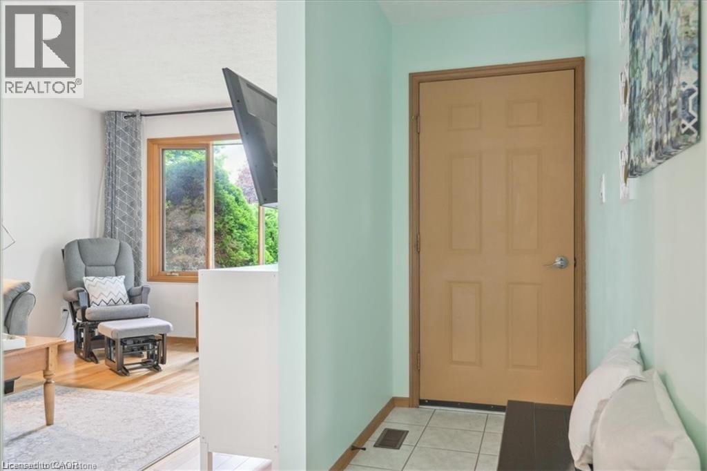 A room with a brown door, a grey chair, and a window with a view of trees.