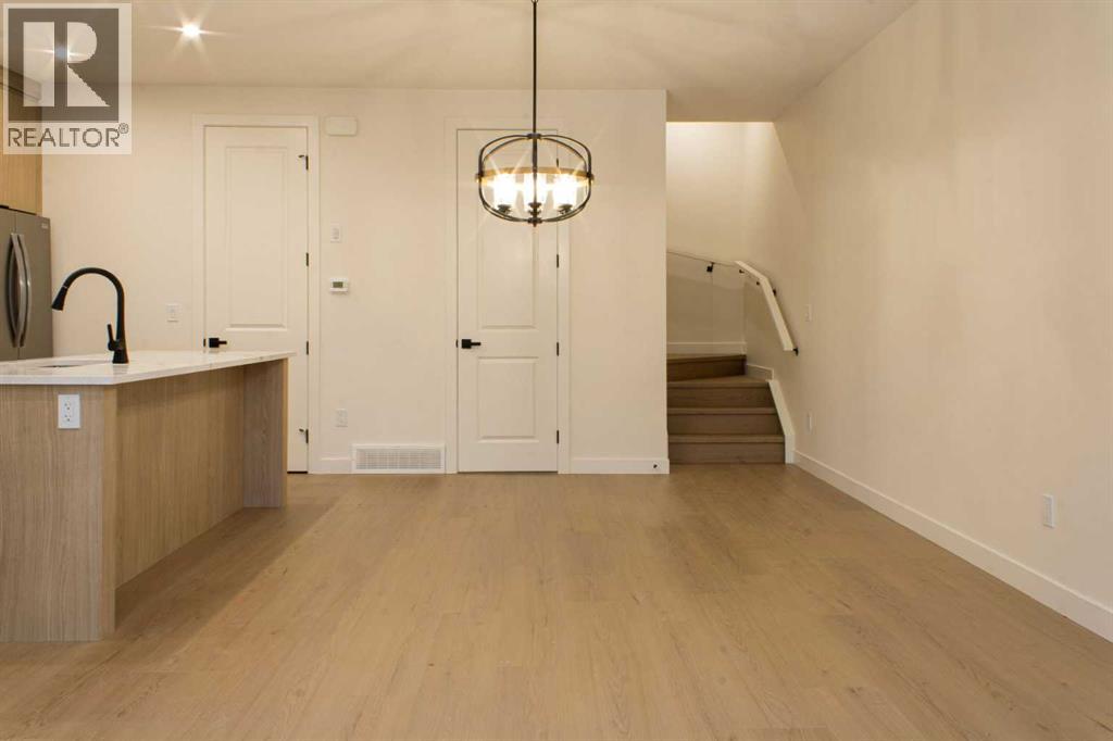 A well-lit kitchen with wooden floors and a staircase in the background.