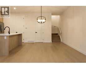 A well-lit kitchen with wooden floors and a staircase in the background.