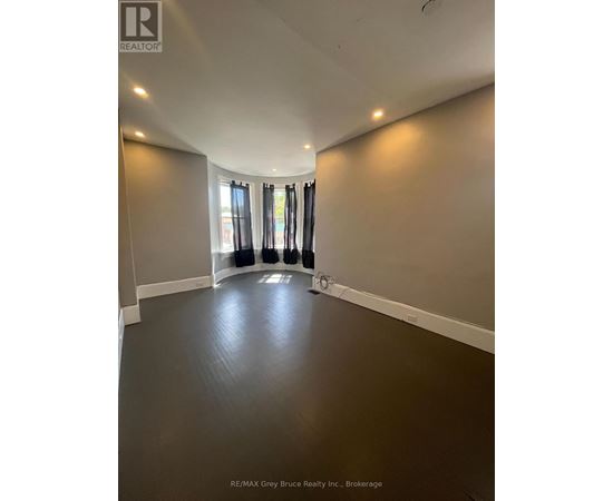 A spacious room with a dark floor and a large window with curtains.
