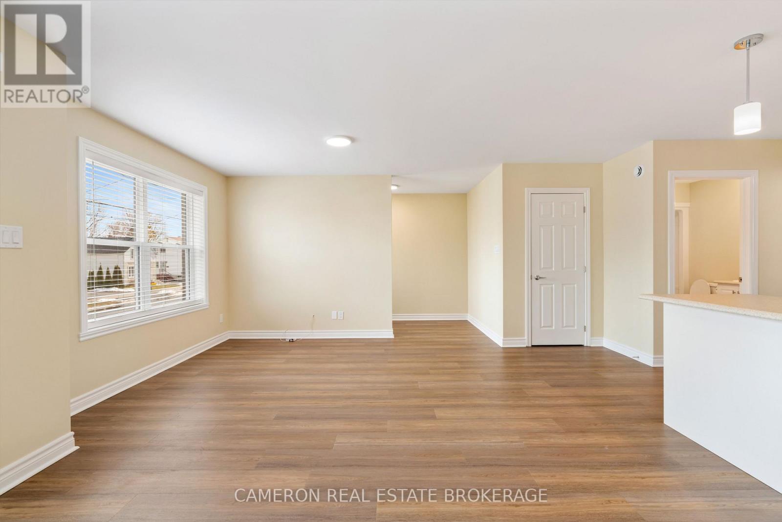 A spacious room with wooden floors and white walls, with a door on the right side.