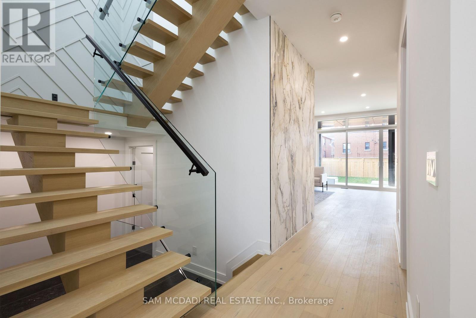 A wooden staircase with glass railings leads to a bright open space.