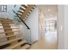 A wooden staircase with glass railings leads to a bright open space.