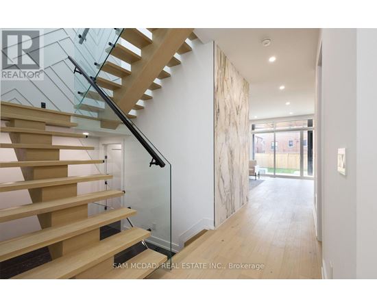 A wooden staircase with glass railings leads to a bright open space.