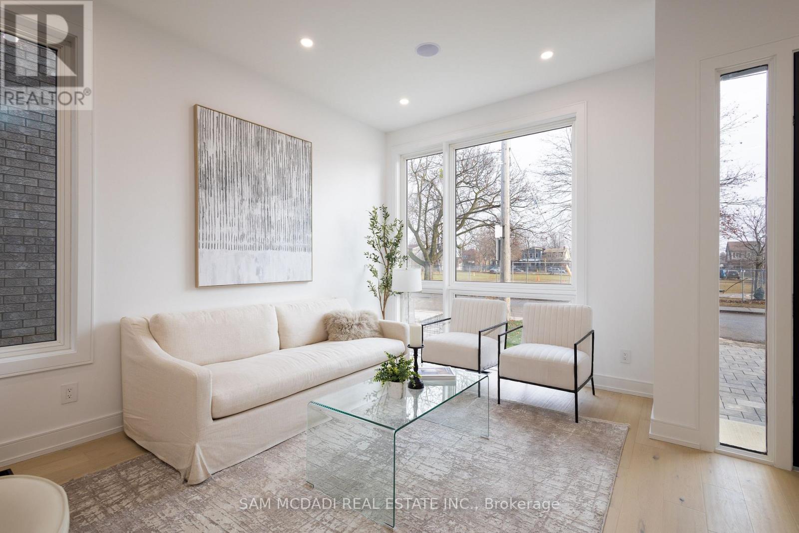 A living room with a white couch, a glass coffee table, and a painting on the wall.
