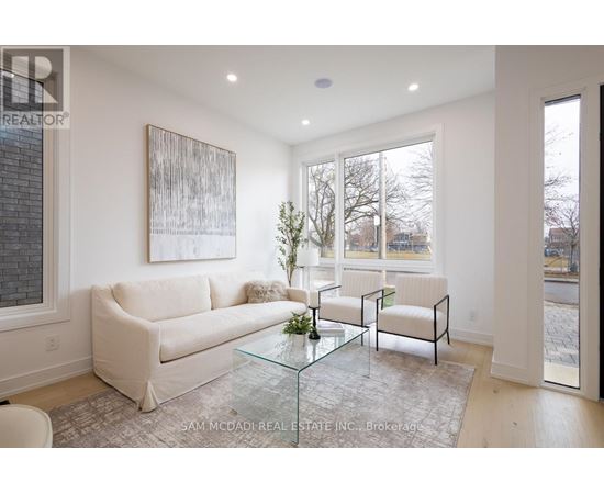 A living room with a white couch, a glass coffee table, and a painting on the wall.