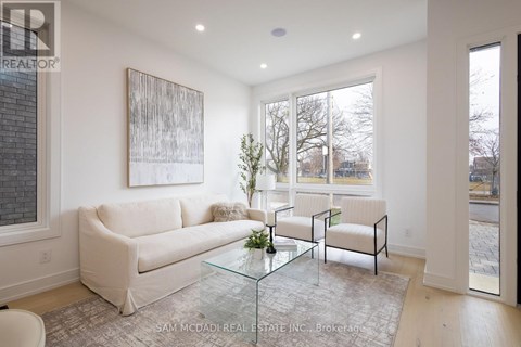A living room with a white couch, a glass coffee table, and a painting on the wall.