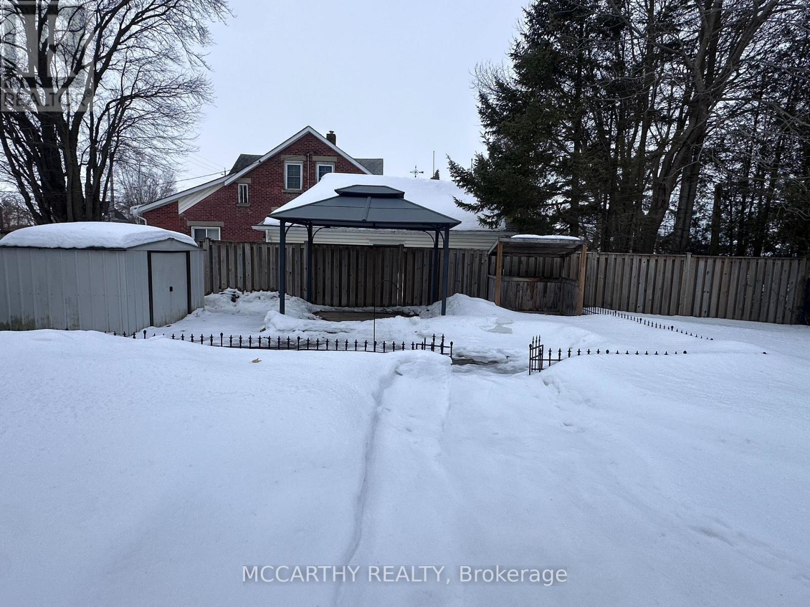 A snow-covered yard with a gazebo and a house in the background.