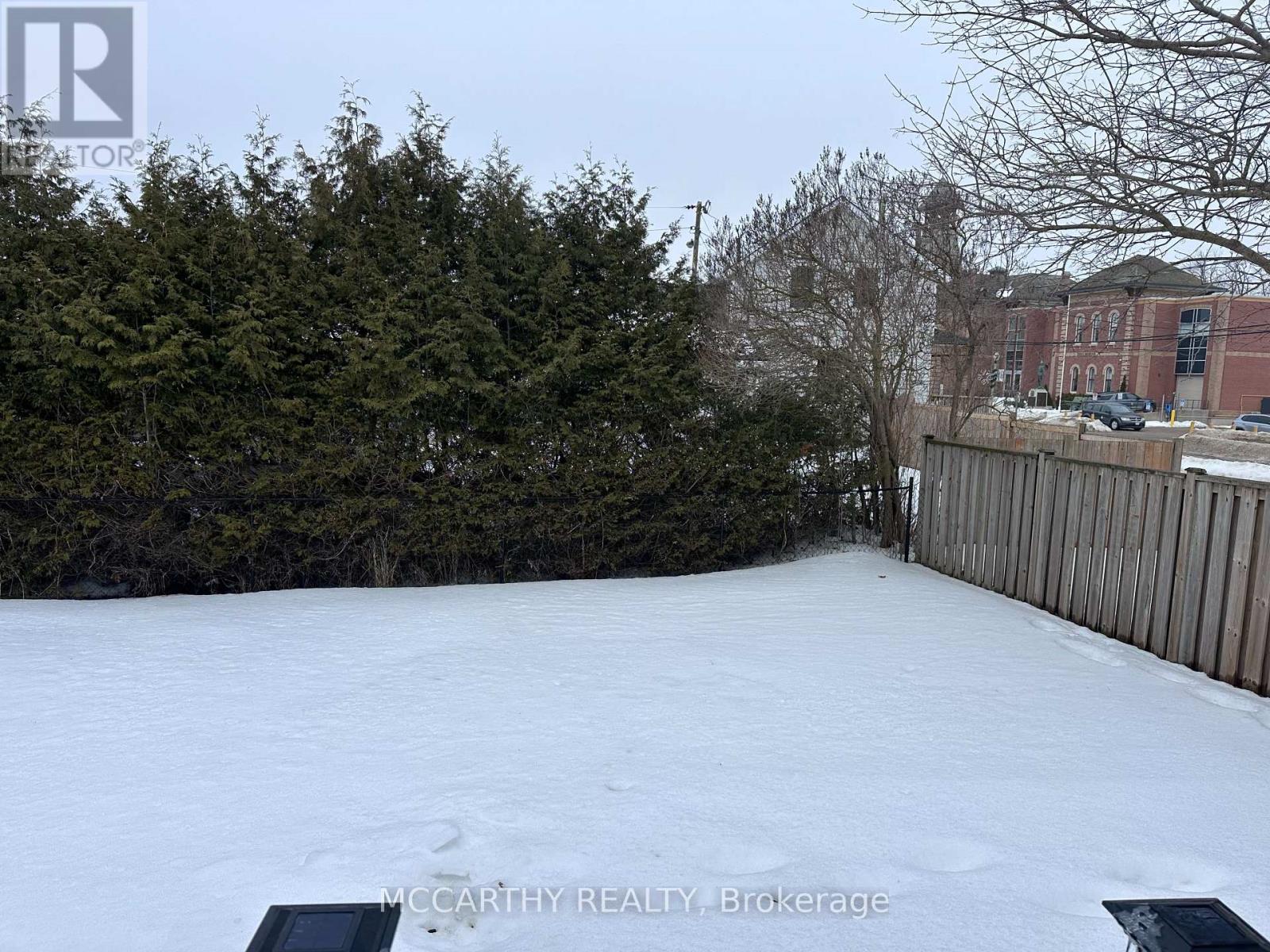 A snow-covered yard with a fence and trees in the background.