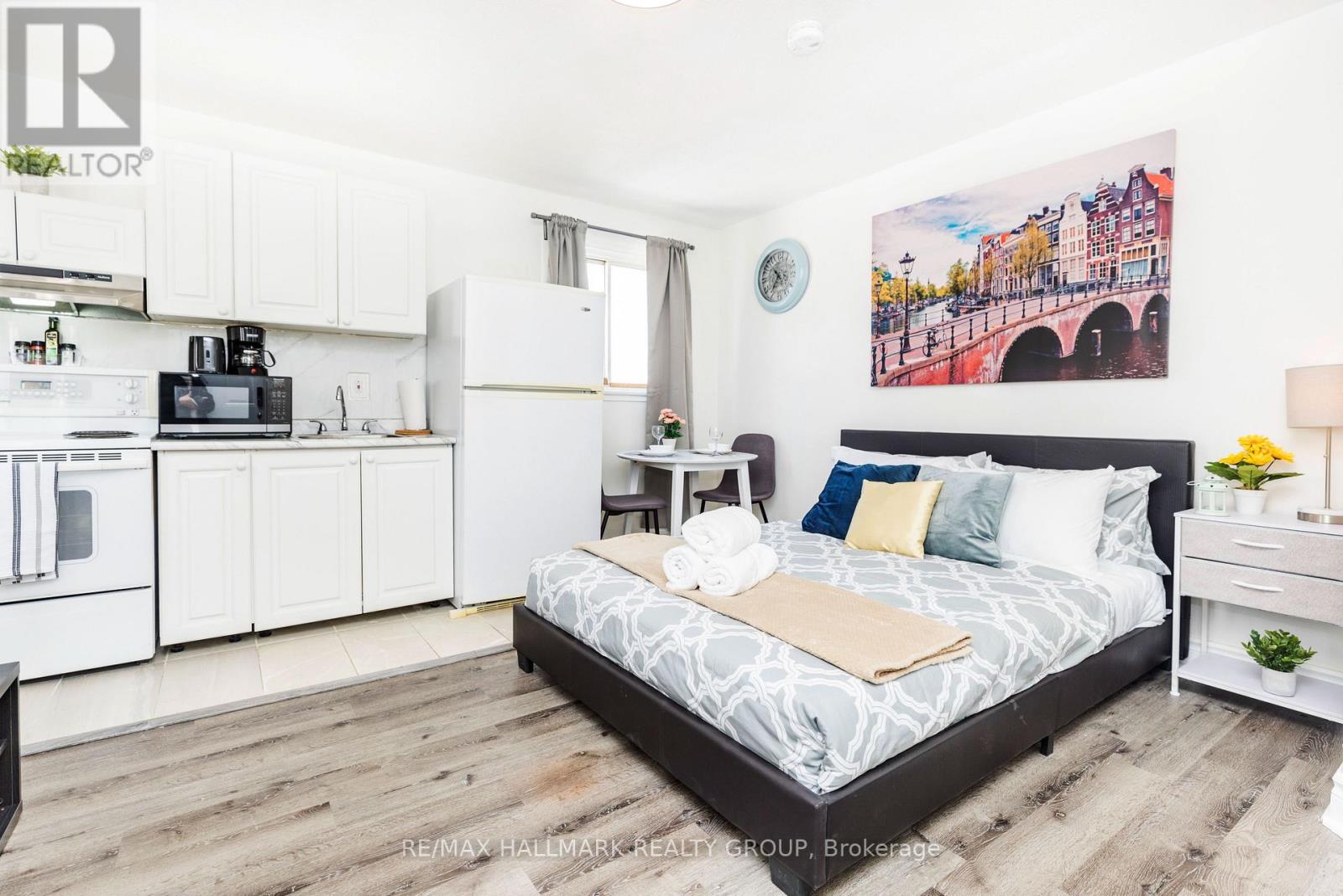 A bedroom with a bed, nightstand, and a painting on the wall.