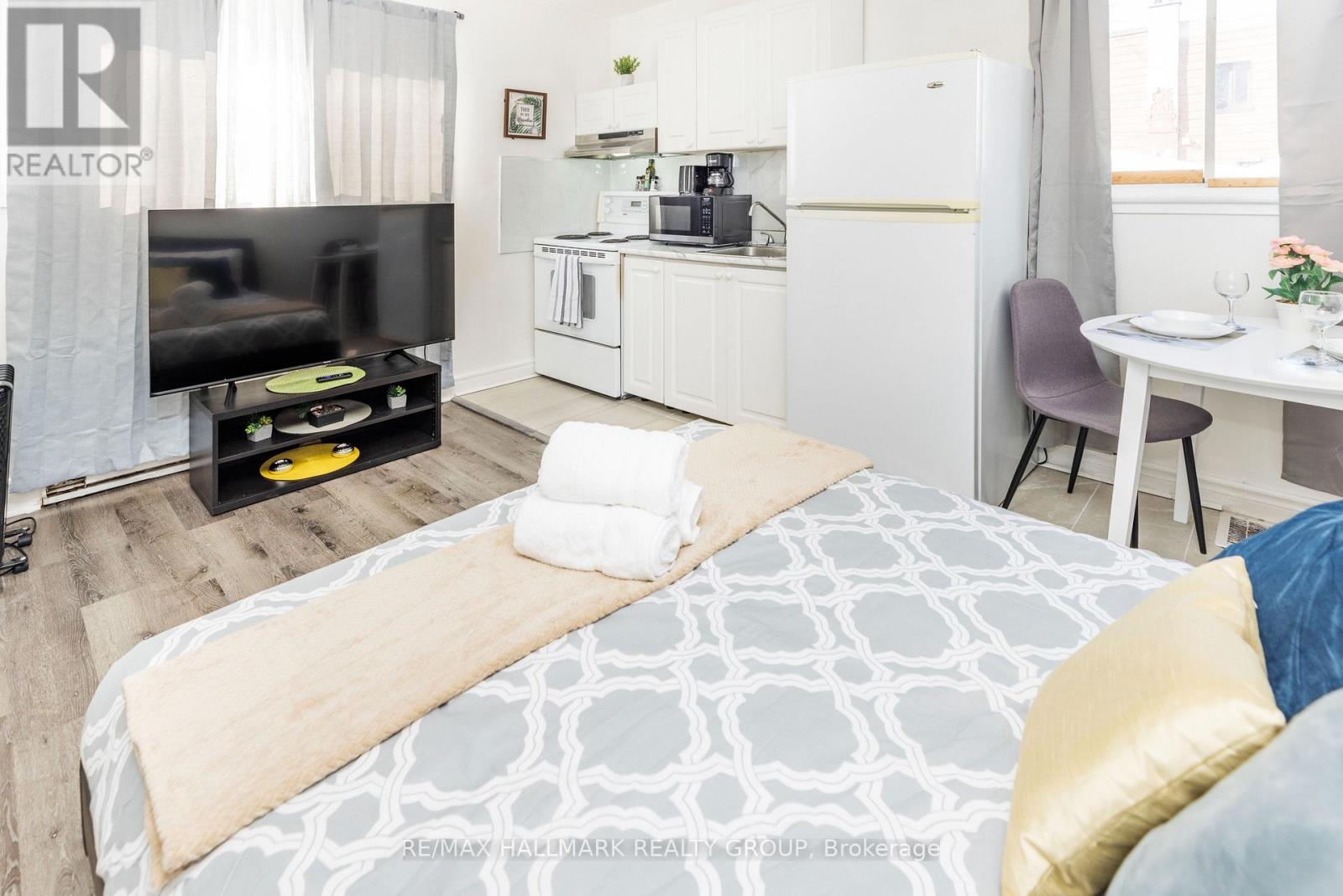 A bedroom with a bed, a TV, a kitchenette, and a dining area.