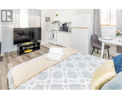 A bedroom with a bed, a TV, a kitchenette, and a dining area.