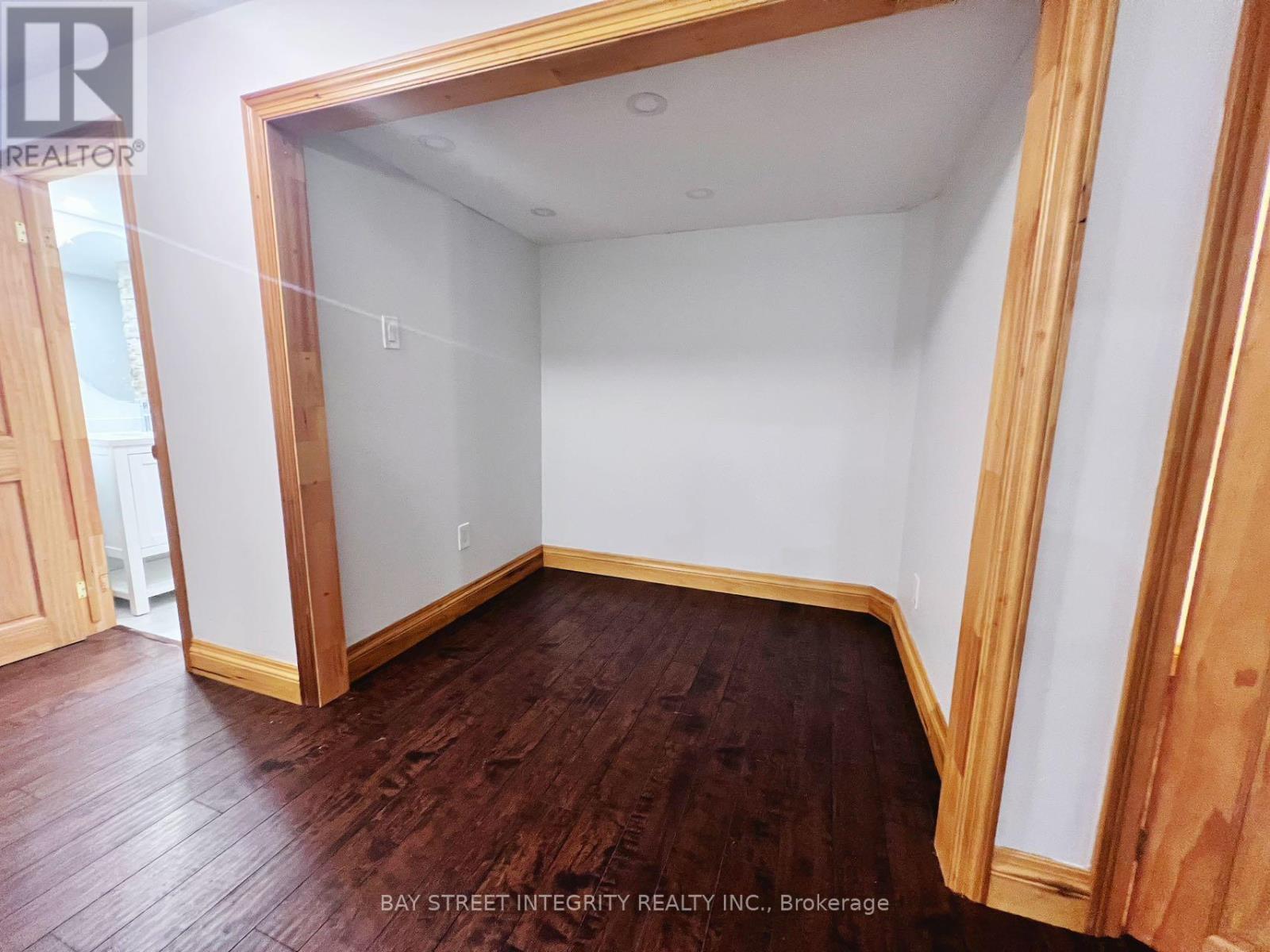 A room with wooden floors and white walls, with a doorway leading to another room.