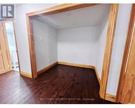 A room with wooden floors and white walls, with a doorway leading to another room.