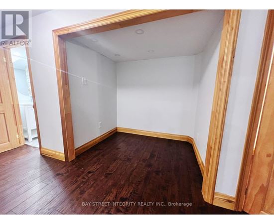 A room with wooden floors and white walls, with a doorway leading to another room.