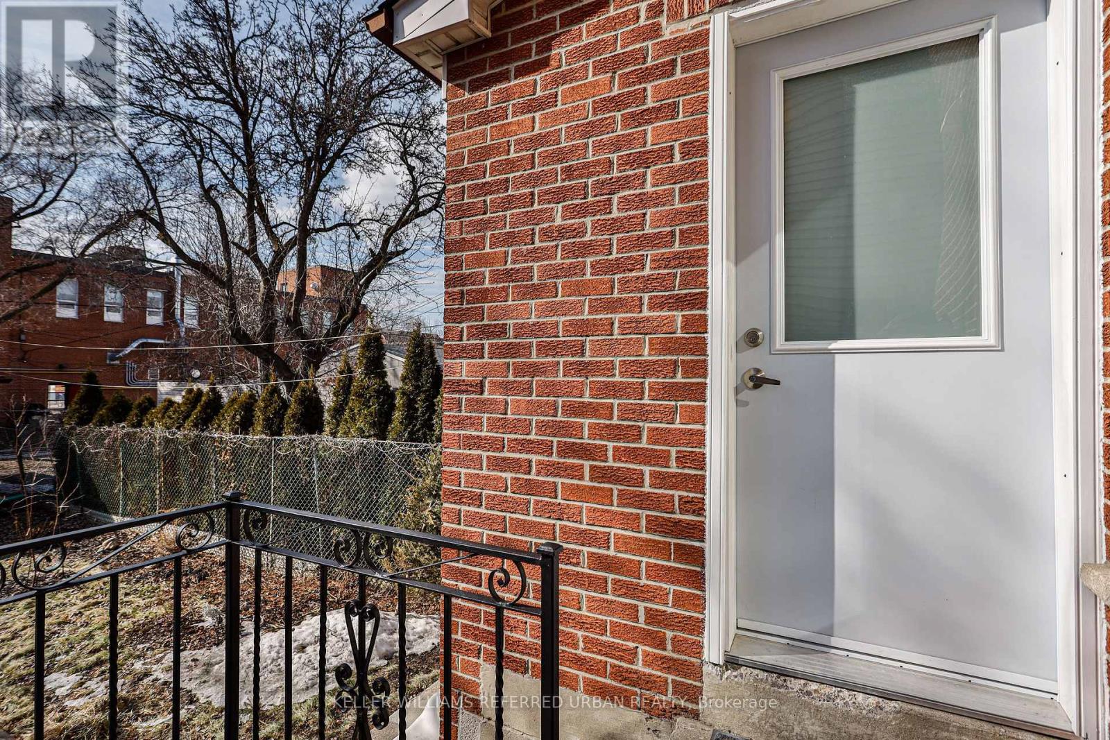 A white door is on a brick wall with a black fence in front.