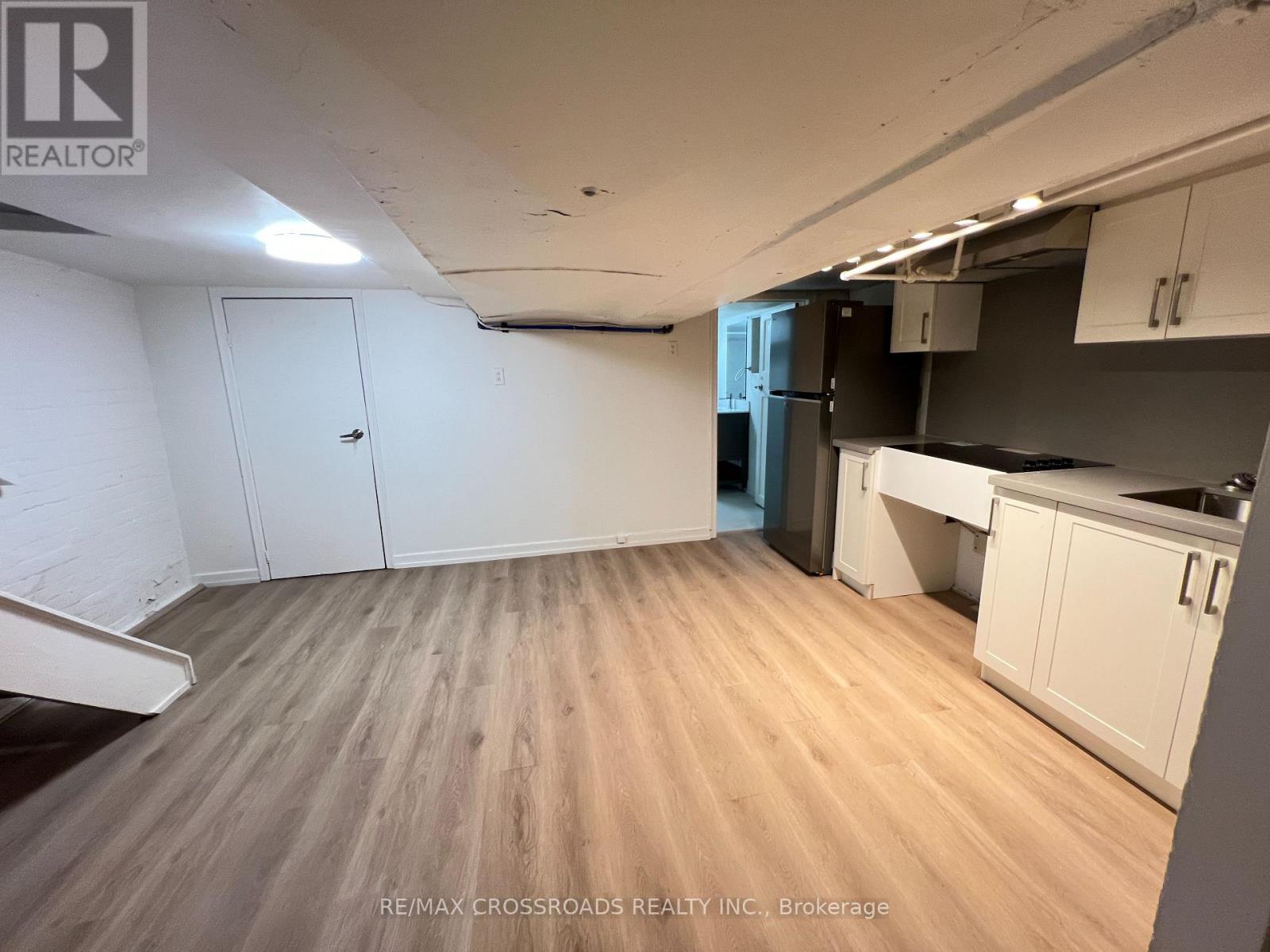 A room with wooden flooring and white walls, with a kitchen area to the right.