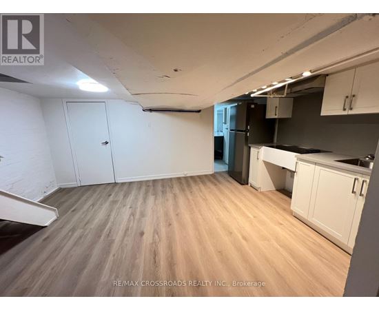 A room with wooden flooring and white walls, with a kitchen area to the right.