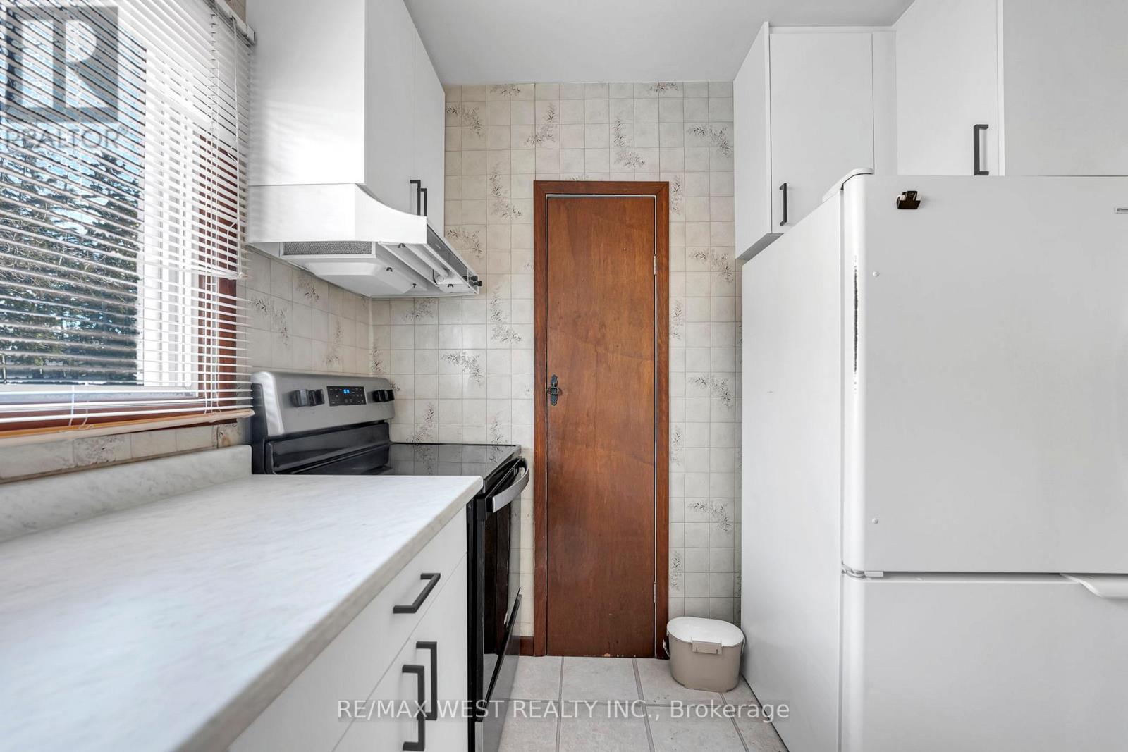 A kitchen with a white fridge, black oven, and wooden door.
