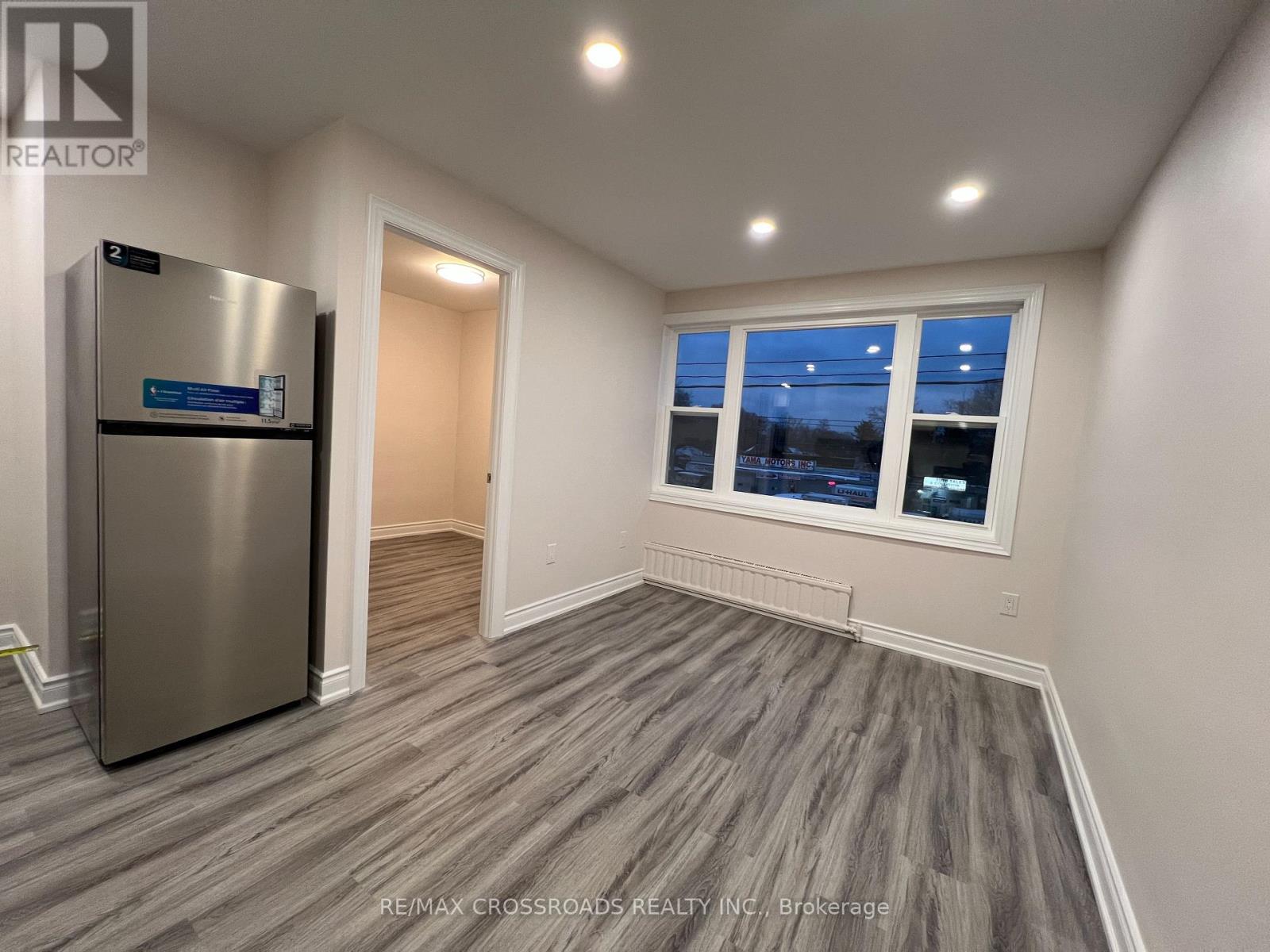 A room with a stainless steel refrigerator and wooden flooring.