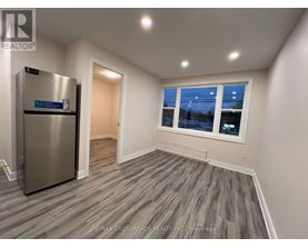 A room with a stainless steel refrigerator and wooden flooring.