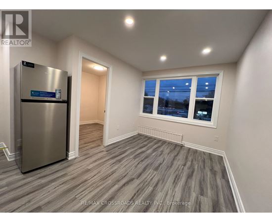 A room with a stainless steel refrigerator and wooden flooring.