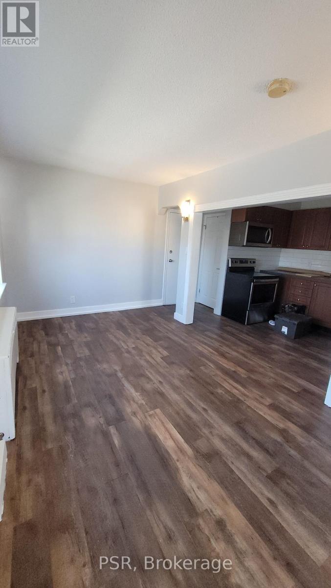 A room with wooden flooring and a kitchen area in the background.