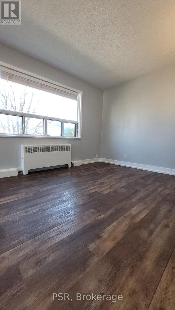 A room with wooden flooring and a window with a radiator beneath it.