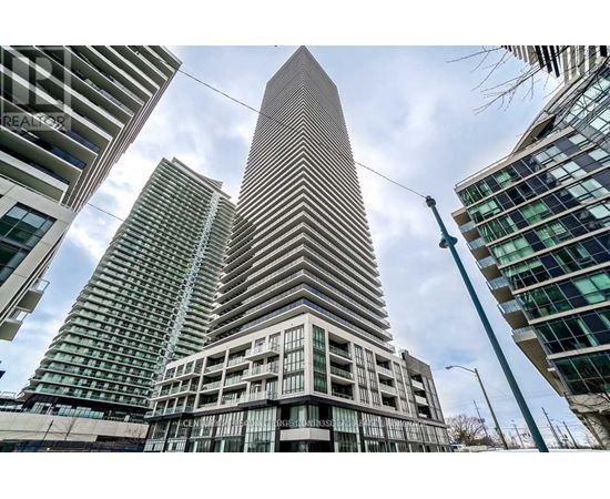 A tall building with a pointed top stands in front of other buildings.