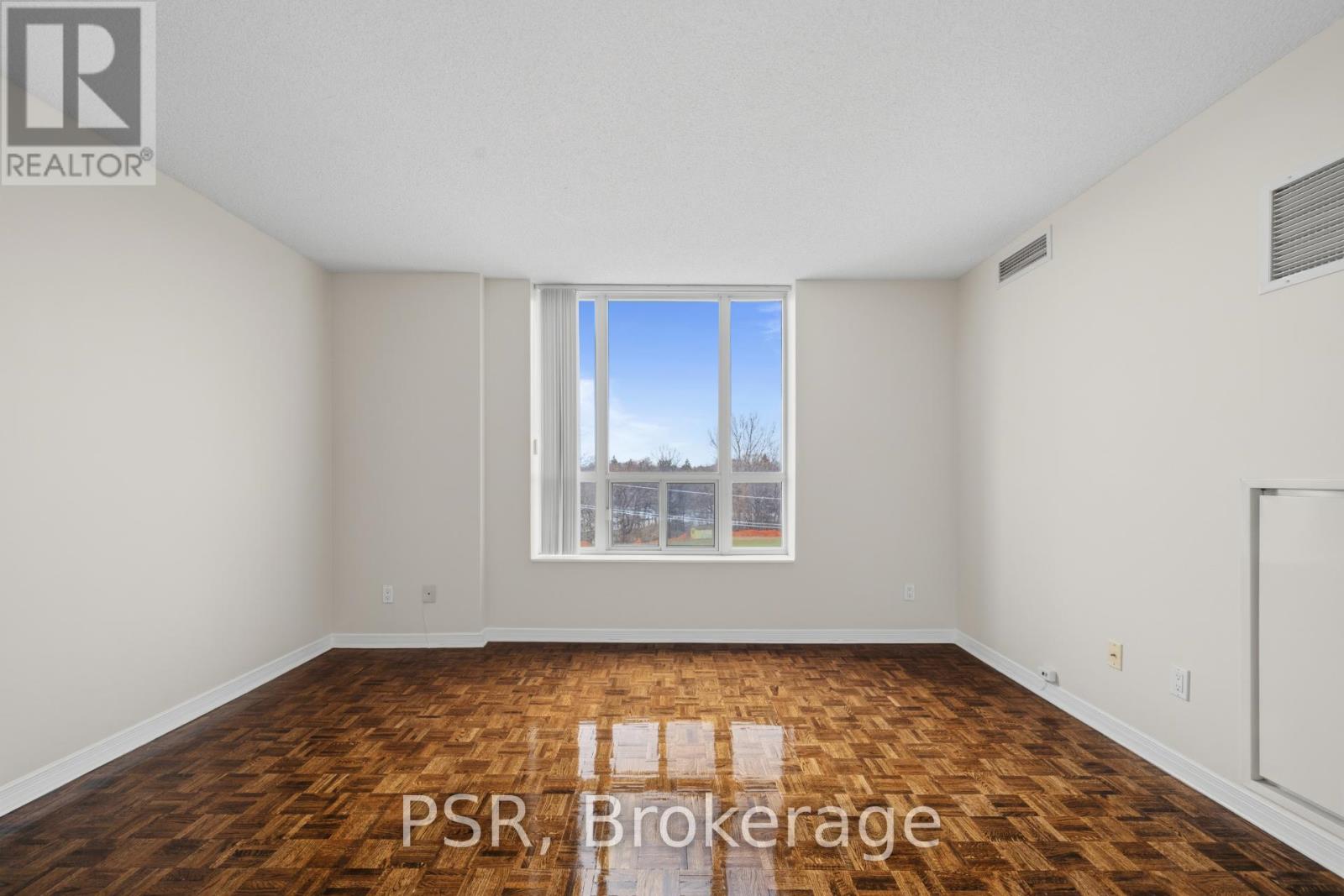 A room with wooden flooring and a large window showing a view of trees and a building.