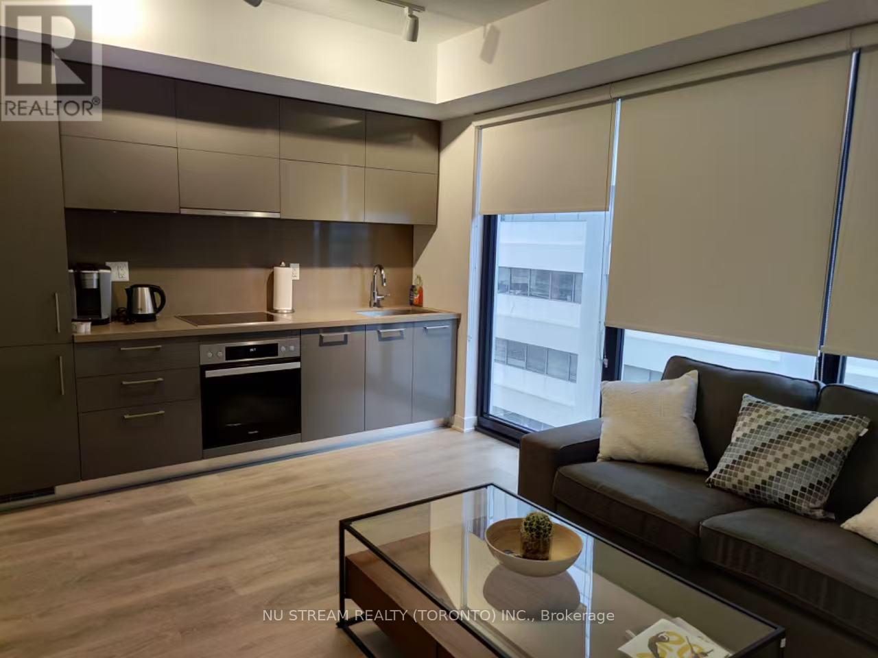 A modern kitchen with a glass table and a couch with pillows.