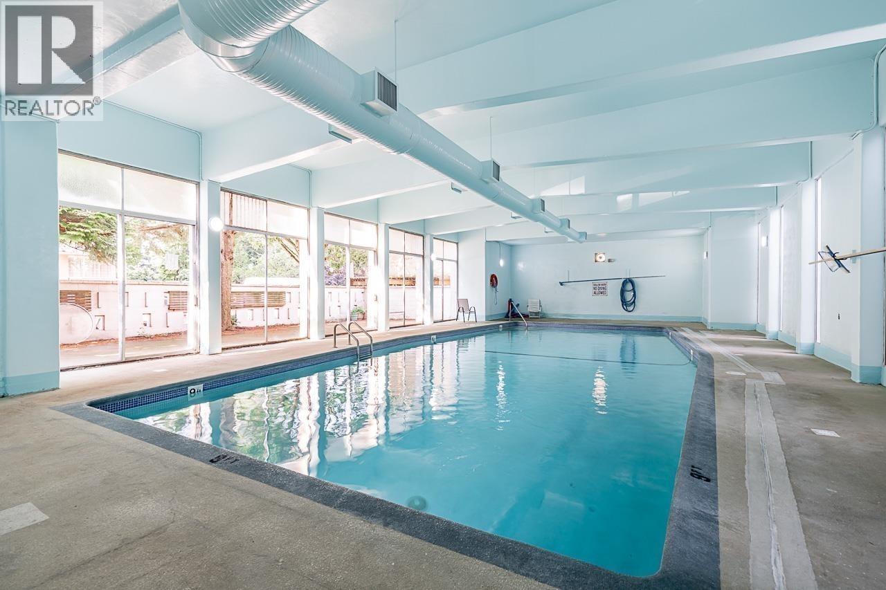 A large indoor swimming pool with a person sitting on the edge.