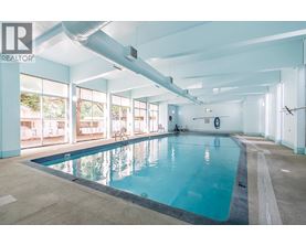 A large indoor swimming pool with a person sitting on the edge.