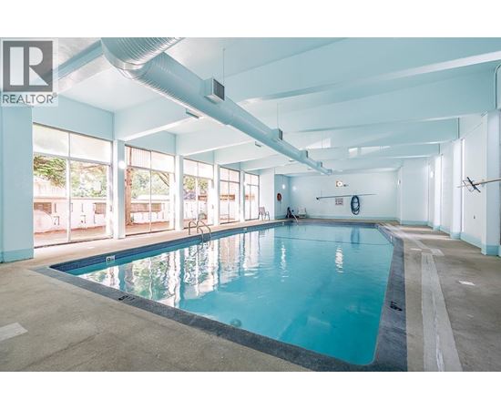 A large indoor swimming pool with a person sitting on the edge.