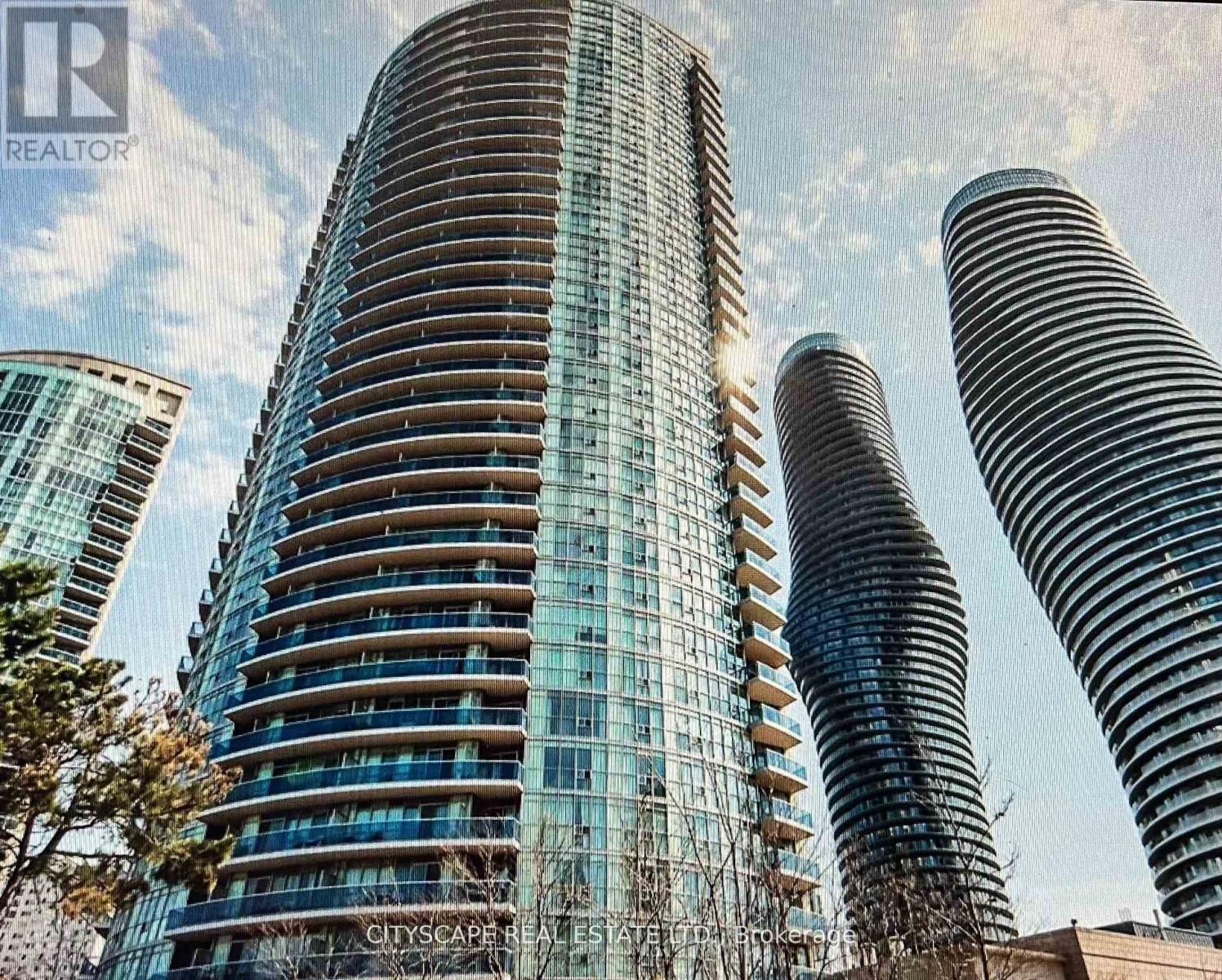 A tall building with a curved glass facade stands in front of two other buildings.