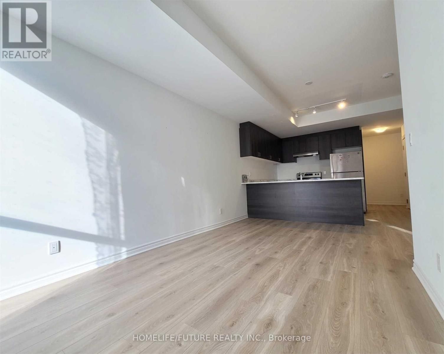 A spacious room with wooden flooring and a kitchen area in the background.