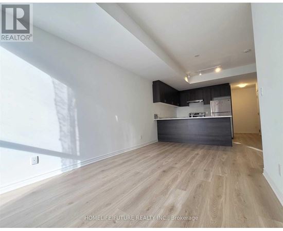 A spacious room with wooden flooring and a kitchen area in the background.