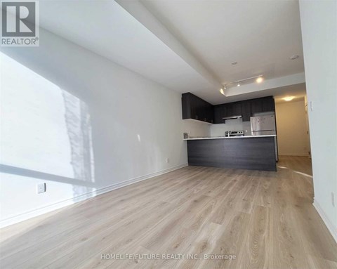 A spacious room with wooden flooring and a kitchen area in the background.
