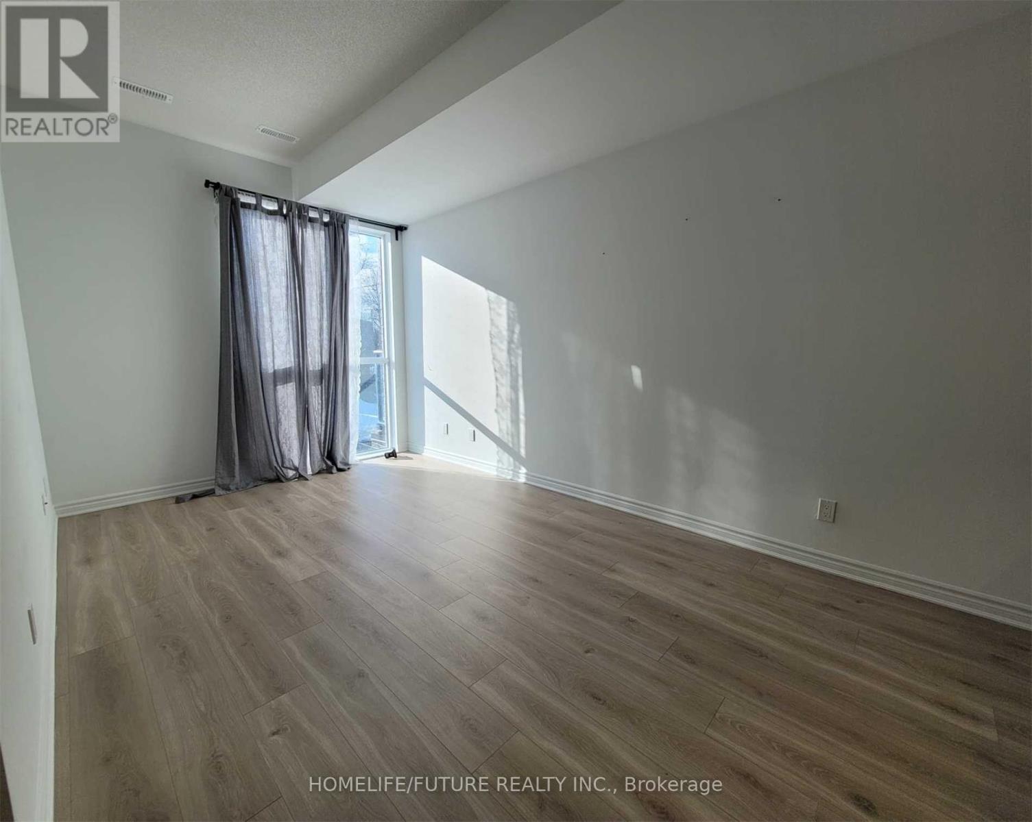 A room with wooden flooring and a window with curtains.