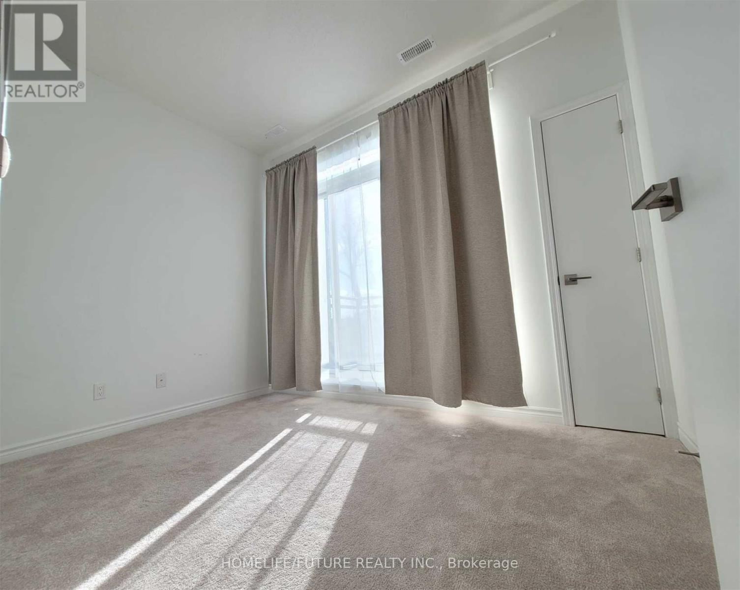 A room with a carpeted floor, a door, and a window with curtains.