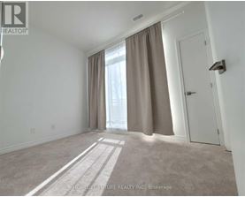 A room with a carpeted floor, a door, and a window with curtains.