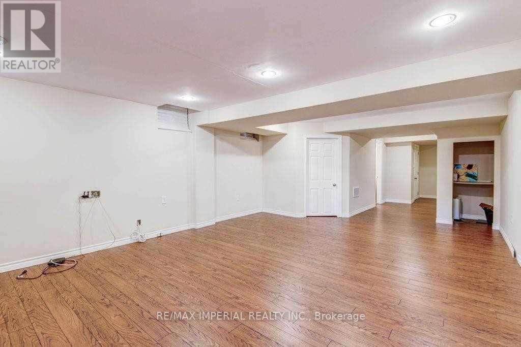 A spacious room with wooden flooring and white walls, with a brokerage logo in the corner.