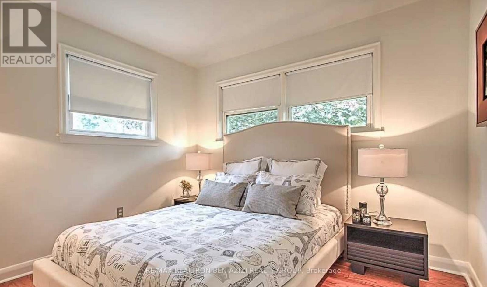 A bedroom with a bed, nightstands, and two windows.
