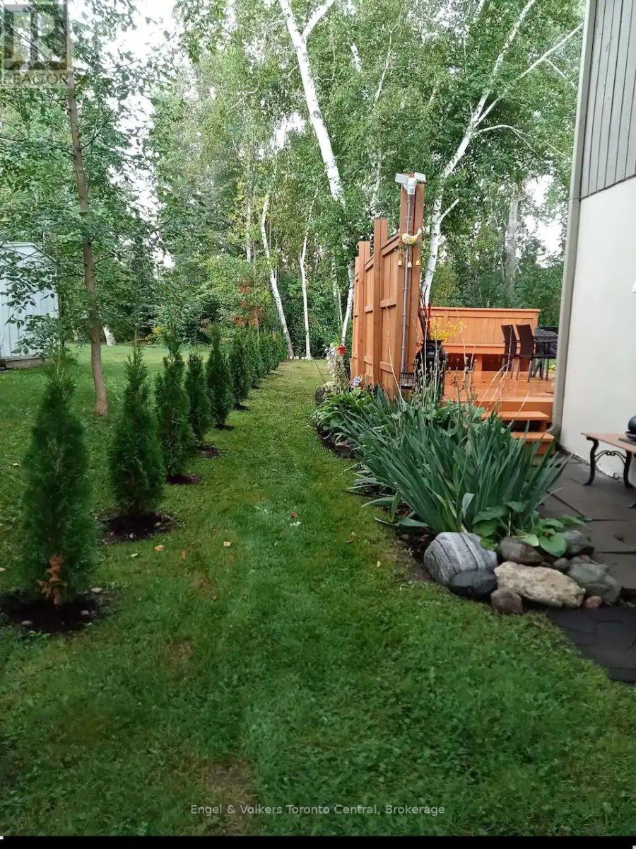 A backyard with a lawn, trees, and a wooden deck.