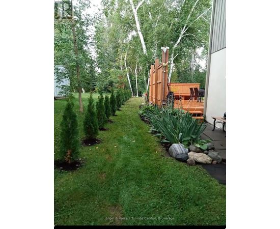 A backyard with a lawn, trees, and a wooden deck.