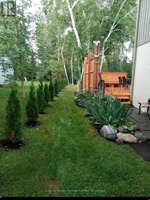 A backyard with a lawn, trees, and a wooden deck.