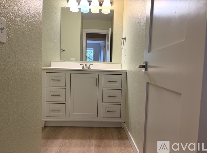 A white cabinet with drawers is in a room with a mirror above it.