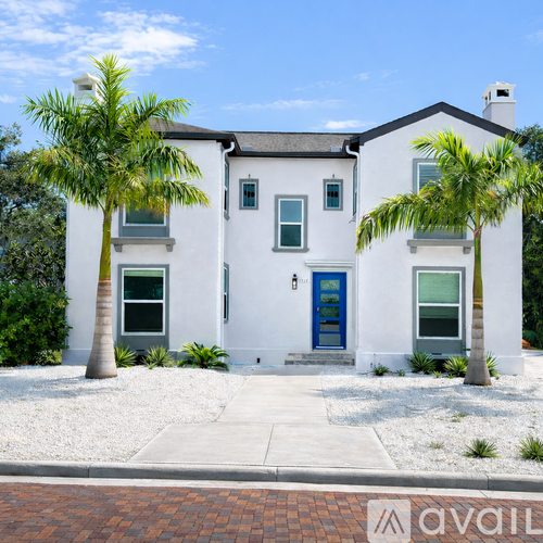 A white house with a blue door and two palm trees in front.
