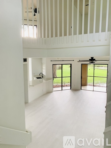 A spacious, white room with a ceiling fan and a view of a green lawn through the windows.